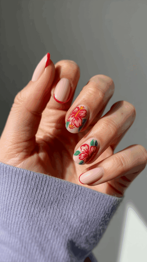 A hand with a manicure featuring light pink nails with red tips, and floral designs with vibrant pink flowers and green leaves on the ring and middle finger.
