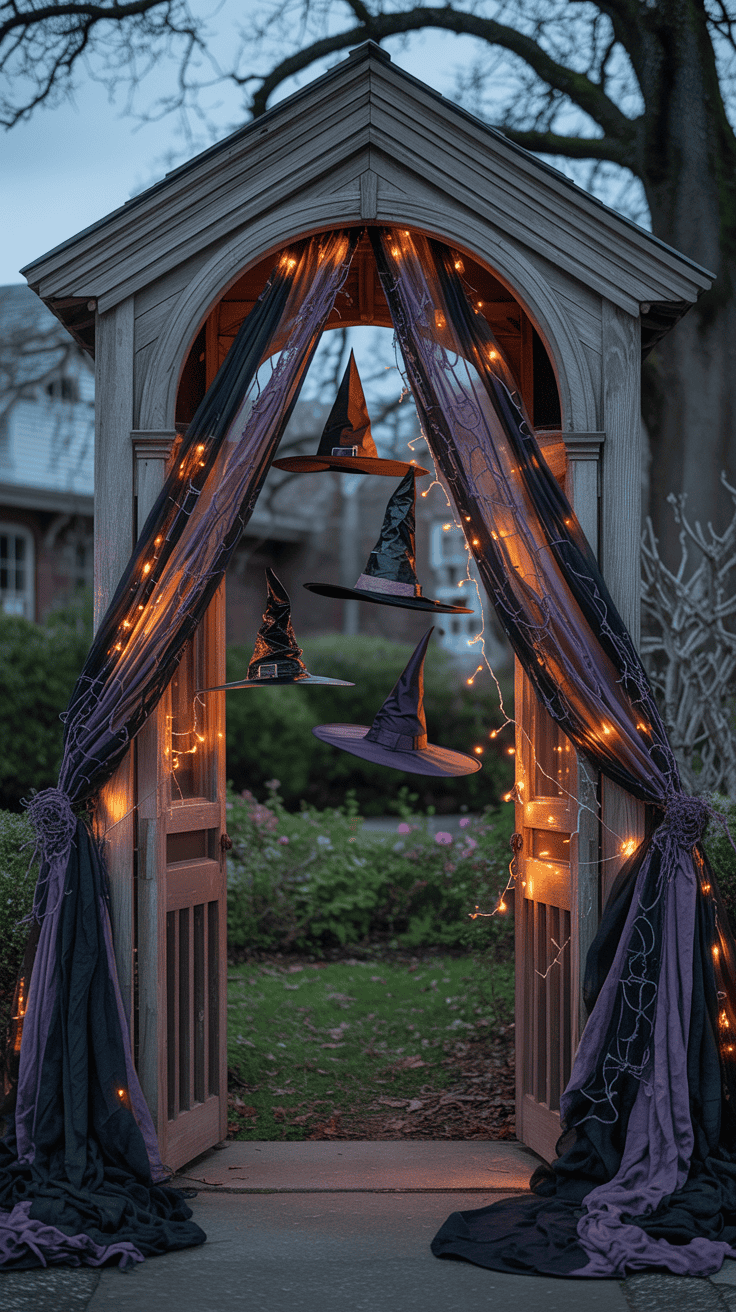 A wooden archway decorated with purple and black drapes and orange fairy lights, featuring hanging witch hats, set in a garden area with plants and trees in the background.