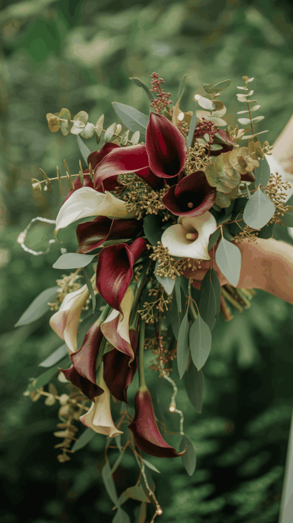 A bouquet of deep burgundy and white calla lilies with eucalyptus leaves, held against a blurred green background.